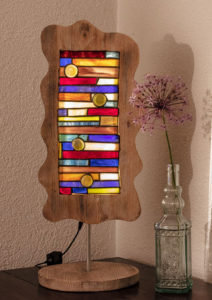Bunte Glaslampe aus Rechtecken und großen Glasnuggets. Rahmen in Wellenform und Vintage Look. Lampe und Lampenfuß sind mit einem Rundeisen miteinander verbunden.