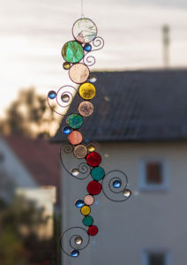 Bunter Sonnenfänger aus vielen kreisrunden, geschnittenen Gläsern, die in der Tiffany-Technik wellenförmig miteinander verbunden sind. Besticht durch eingearbeitete, spiralförmige, filigranen Drahtelementen mit kleinen Glasnuggets.